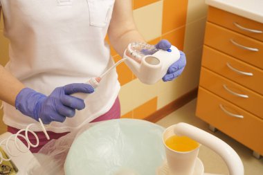 Genç dişçi kadının ağız sulandırıcısı var. Kapalı alan, ofis arka planı, fotokopi alanı, iç çekim. Çene modeli. Doktor hasta sulama eylemi gösteriyor