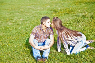 Parkta yeşil çimlerde oturan ve öpüşen mutlu bir İspanyol çiftin portresi.