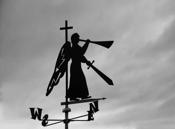 silhouette of iron trumpeting Angel with sword and trumpet. weather vane on roof of house. blue sky background. Christian angel of the apocalypse