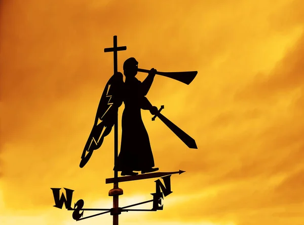 silhouette of iron trumpeting Angel with sword and trumpet. weather vane on roof of house. sunset yellow  sky background. Christian angel of the apocalypse