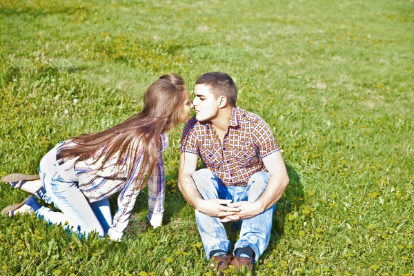 一对快乐的年轻夫妇坐在公园的绿草上亲吻的画像 — 图库照片