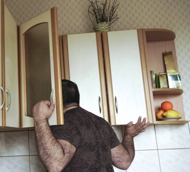 Gömlekli genç adam evde mutfak dolabına gizlice bakıyor, arkadan bakıyor. Yalnız, aç erkek, bekar, yiyecek arayan.. 