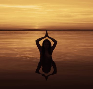 Siluet genç kadın sahilde yoga yapıyor. Eller yukarı.. 