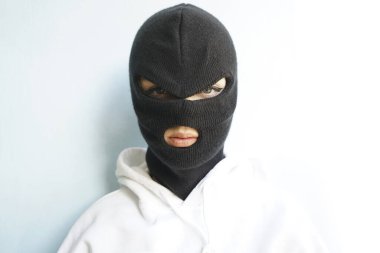 Beyaz kapüşonlu, kar maskeli ya da siyah maskeli bir kadın beyaz ya da mavi duvar arkasında izole edilmiş. . 