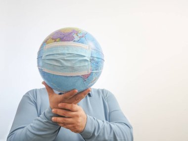 Dünya Salgın Tehlikesi. Dünya 'nın, beyaz bir arka planda izole edilmiş yüz maskesi ve elleriyle Dünya' yı korumaya ihtiyacı var. İnsan salgını tehlikesi. Erkek yüzünün arkasında virüs maskesi olan dünya haritası. 