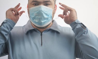 Onu Coronavirus 'tan koruyacak maskeli bir adam. Corona virüsü salgını. Adam maske takıyor. Maskeli genç adam ayakta duruyor. Kapüşonlu, tıbbi maskeli biri. beyaz arkaplanda izole