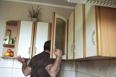Gömlekli genç adam evde mutfak dolabına gizlice bakıyor, arkadan bakıyor. Yalnız, aç erkek, bekar, yiyecek arayan.. 
