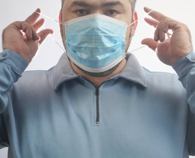 Onu Coronavirus 'tan koruyacak maskeli bir adam. Corona virüsü salgını. Adam maske takıyor. Maskeli genç adam ayakta duruyor. Kapüşonlu, tıbbi maskeli biri. beyaz arkaplanda izole