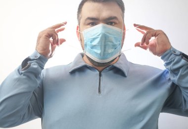 Onu Coronavirus 'tan koruyacak maskeli bir adam. Corona virüsü salgını. Adam maske takıyor. Maskeli genç adam ayakta duruyor. Kapüşonlu, tıbbi maskeli biri. beyaz arkaplanda izole.