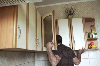 Gömlekli genç adam evde mutfak dolabına gizlice bakıyor, arkadan bakıyor. Yalnız, aç erkek, bekar, yiyecek arayan.. 