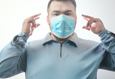 Onu Coronavirus 'tan koruyacak maskeli bir adam. Corona virüsü salgını. Adam maske takıyor. Maskeli genç adam ayakta duruyor. Kapüşonlu, tıbbi maskeli biri. beyaz arkaplanda izole.