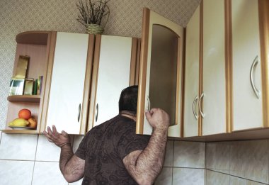 Gömlekli genç adam evde mutfak dolabına gizlice bakıyor, arkadan bakıyor. Yalnız, aç erkek, bekar, yiyecek arayan.. 
