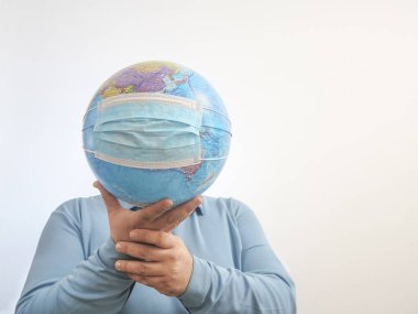 Dünya Salgın Tehlikesi. Dünya 'nın, beyaz bir arka planda izole edilmiş yüz maskesi ve elleriyle Dünya' yı korumaya ihtiyacı var. İnsan salgını tehlikesi. Erkek yüzünün arkasında virüs maskesi olan dünya haritası. 