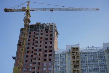 İnşaat alanı. İnşaat alanında çalışan bir vinç, bir ev inşaatı. Arkadaki mavi gökyüzü. 