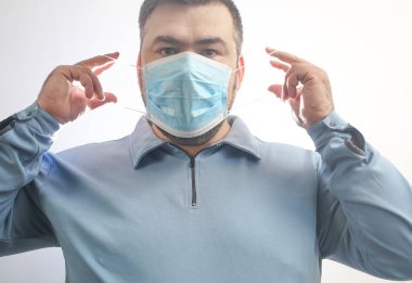 Onu Coronavirus 'tan koruyacak maskeli bir adam. Corona virüsü salgını. Adam maske takıyor. Maskeli genç adam ayakta duruyor. Kapüşonlu, tıbbi maskeli biri. beyaz arkaplanda izole.