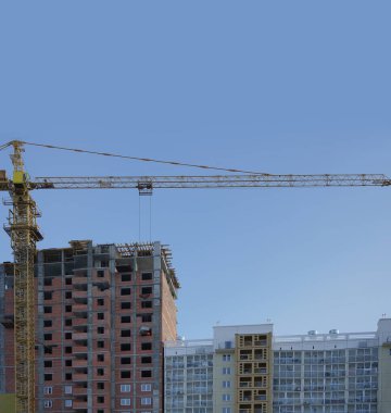 İnşaat alanı. İnşaat alanında çalışan bir vinç, bir ev inşaatı. Arkadaki mavi gökyüzü. 