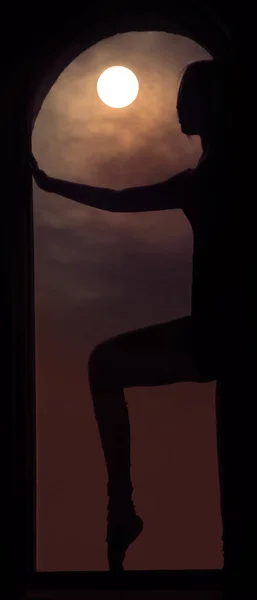 巨大な窓の上に立つ若いいい女のシルエット 満月の力の概念 丸い窓枠の間に立つ美しい女の子 真夜中の月明かり — ストック写真