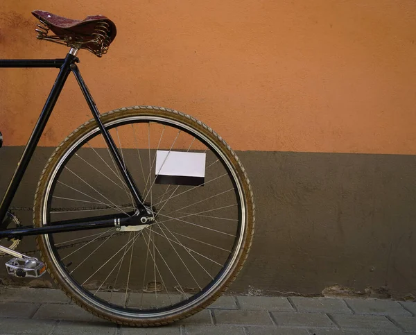 茶色とオレンジの壁の背景にスタイリッシュな古いスタイルの黒い自転車 自転車は外に停めた セメントの壁の背景 スポーク間の空のポストカード — ストック写真