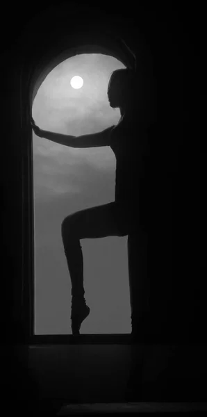 silhouette of a young good shaped woman standing on the huge window. Concept of full moon power. Beautiful girl standing between round window frame. midnight moon light.