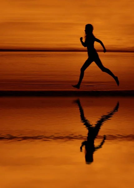 Silhouette of woman jogger running on sunset beach with reflection. slim figure of girl jogging on sea beach at sunset. female jogging along ocean shore during sunrise. exercising outdoor. Healthy active workout lifestyle at nature