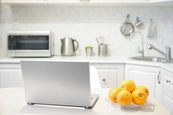 laptop on white modern wooden table in the kitchen. plate with many fruits - oranges.wireless computer Laptop  on gray table with kitchen background. no people