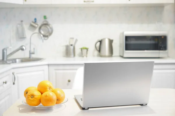 laptop on white modern wooden table in the kitchen. plate with many fruits - oranges.wireless computer Laptop  on gray table with kitchen background. no people