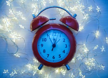 Kırmızı alarmlı saati Noel zamanı kapatma zamanı gece yarısıdır. Işık çelengi ve boş fotokopi alanı olan parlak, altın soyut bir arka plan üzerinde..