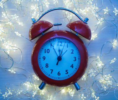 Kırmızı alarmlı saati Noel zamanı kapatma zamanı gece yarısıdır. Işık çelengi ve boş fotokopi alanı olan parlak, altın soyut bir arka plan üzerinde..