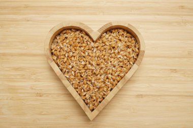 Kırsal ahşap arka planda kalp şeklindeki kasede buğday filizleri ve metin için boş bir alan. Üst manzara, düz uzanma.