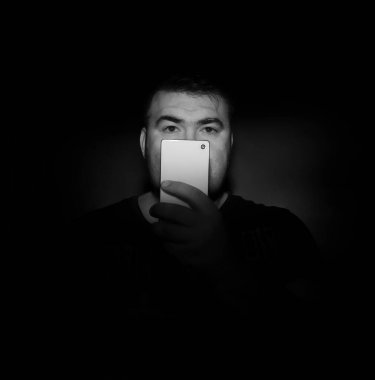 Yakışıklı orta yaşlı bir adam cep telefonuyla çok uzaklara bakıyor siyah arka planda siyah gömlekli. Beyaz cep telefonu. Stüdyo çekimi