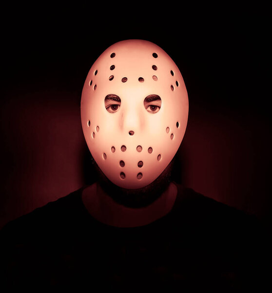 Scary hockey white mask  on young man isolated on black background. nightmare in dark. night scene