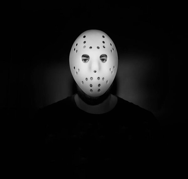 Scary hockey white mask  on young man isolated on black background. nightmare in dark. night scene