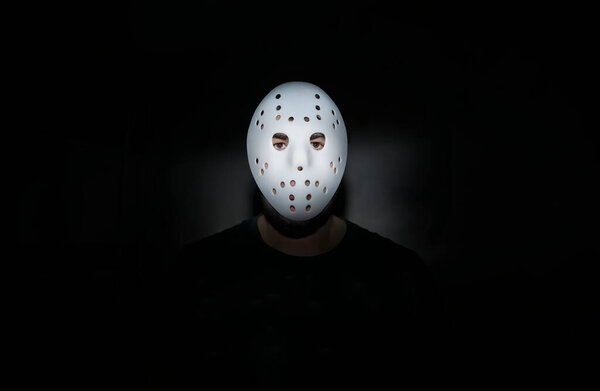 Scary hockey white mask  on young man isolated on black background. nightmare in dark. night scene