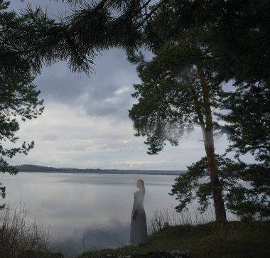 Siluet kadın çam ağacının altında deniz kıyısında tek başına duruyor. Seyahat yeri. yaz tatili.