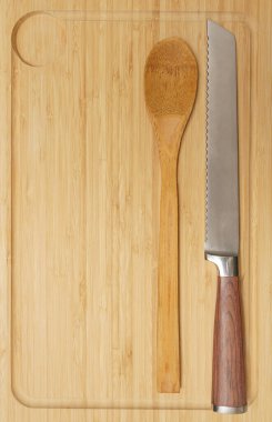 Yeni dikdörtgen tahta tabak, demir bıçak ve tahta kaşık. Ahşap masa arka planında gayri resmi masa ayarları. Ahşap masa üstünde kırsal çatal bıçak takımı