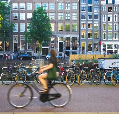 Bulanık yeşil elbiseli genç bir kadın Amsterdam, Hollanda 'da bisiklet sürüyor. 