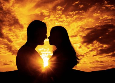 Bir kadın ve erkeğin yakın plan bir silueti. Yüz yüze. Gün batımında sarılan sevgi dolu bir çiftin silueti. Birbirine aşık çiftler. Gün batımı. Romantik akşam.