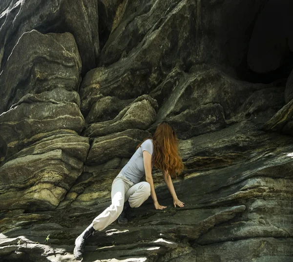 A young woman climbs on an stone wall. It`s a sunny day in the Alps. She loves the andrenaline kick. girl climbs a big stone wall. It is early in the morning, the sun is shining and the woman is wearing blue clothes.