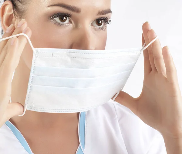 Head and shoulders portrait of hispanic female doctor wearing protective mask and looking at camera posing against white background.