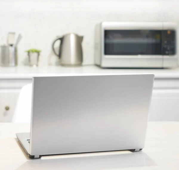 laptop on white modern wooden table in the kitchen. plate with many fruits - oranges. wireless computer Laptop  on gray table with kitchen background. no people