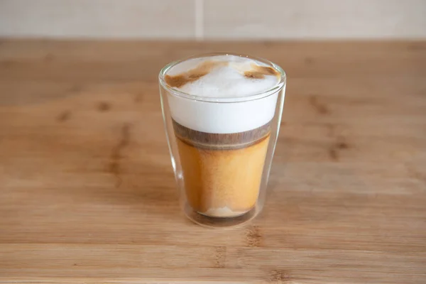 Café multicapa o capuchino en una taza de vidrio sobre una mesa de madera — Foto de Stock