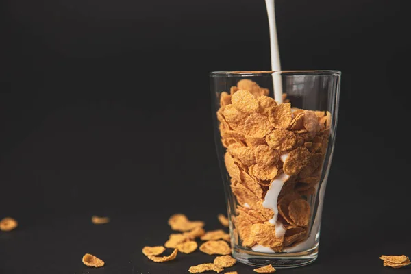 Cornflakes with milk in a transparent glass against a black background — Stock Photo, Image