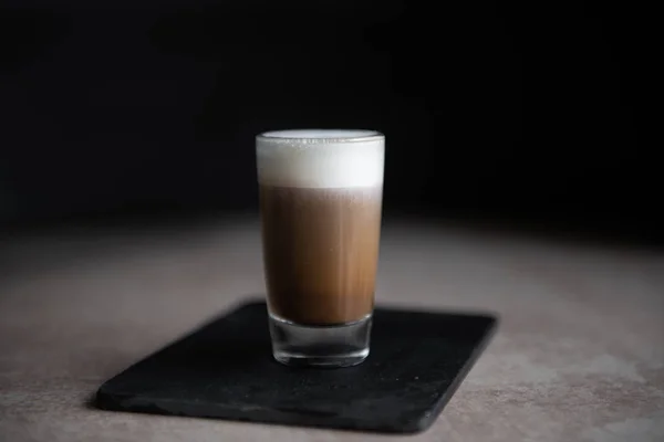 Mini taza de capuchino en una taza de vidrio sobre fondo negro y mesa ligera —  Fotos de Stock