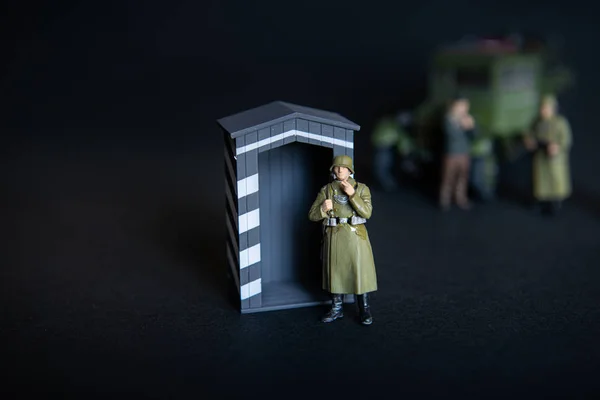 A figure of a man in a military German uniform. In the background of a vague truck