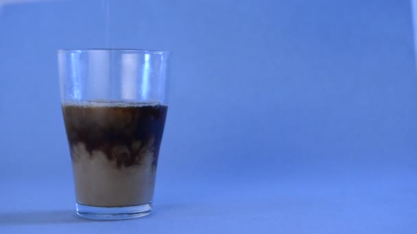 In a glass with black coffee add milk on a blue background with place for text — Stock Video