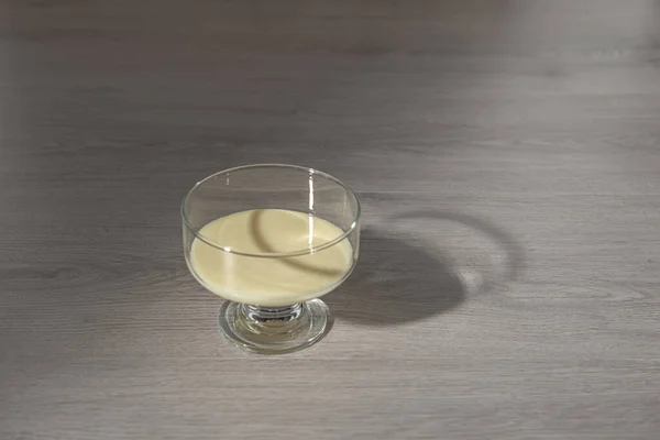 Latte condensato in una ciotola di vetro trasparente su uno sfondo di legno — Foto Stock