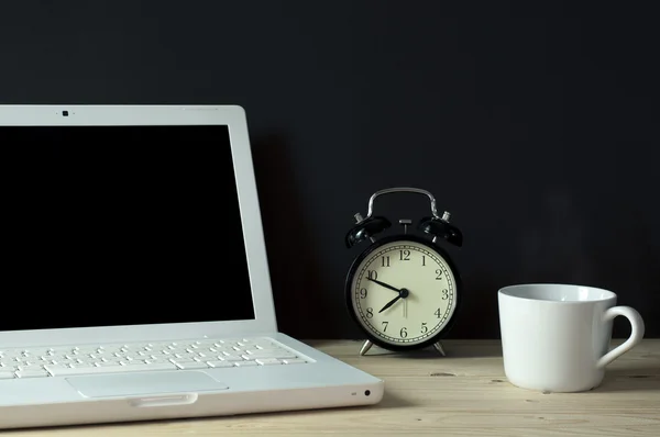 Arbeitsplatz mit leerem Bildschirm-Laptop, Tasse Kaffee und Retro-Alram-Uhr auf dem Tisch. — Stockfoto