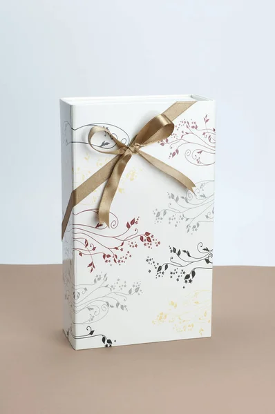 Gift box with golden ribbon bow on light brown and white background. — Stock Photo, Image