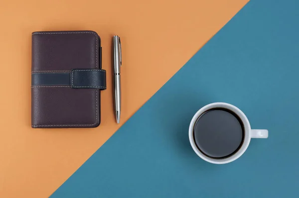 Note book pen and coffee on orange cross light blue pastel background,Top view,Flat lay.