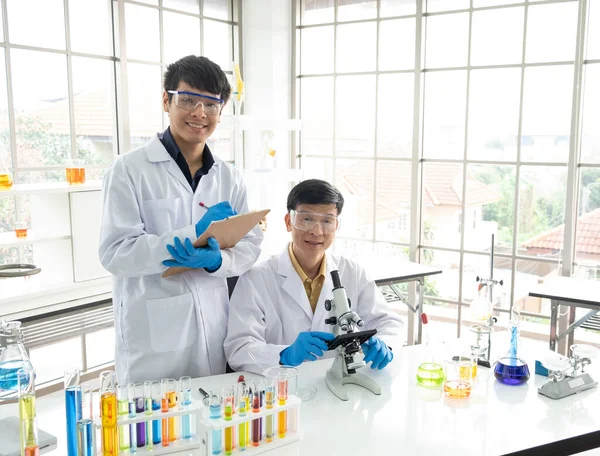 Bilim, Kimya, Teknoloji, Biyoloji ve Laboratuar Konsepti - Asyalı genç bilim adamının portresi notlar alıyor ve Asyalı kıdemli bilim adamı mikroskopuyla çalışıyor.